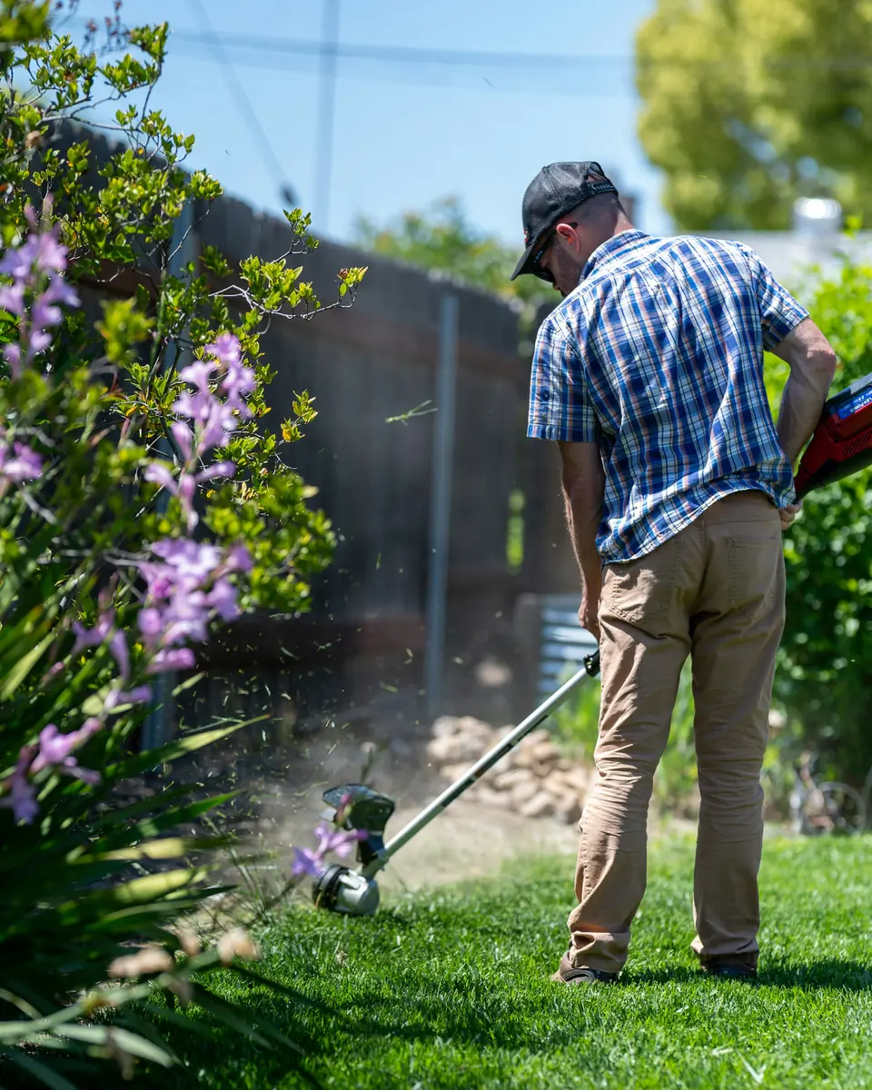 Giardiniere che rifinisce il prato con il decespugliatore